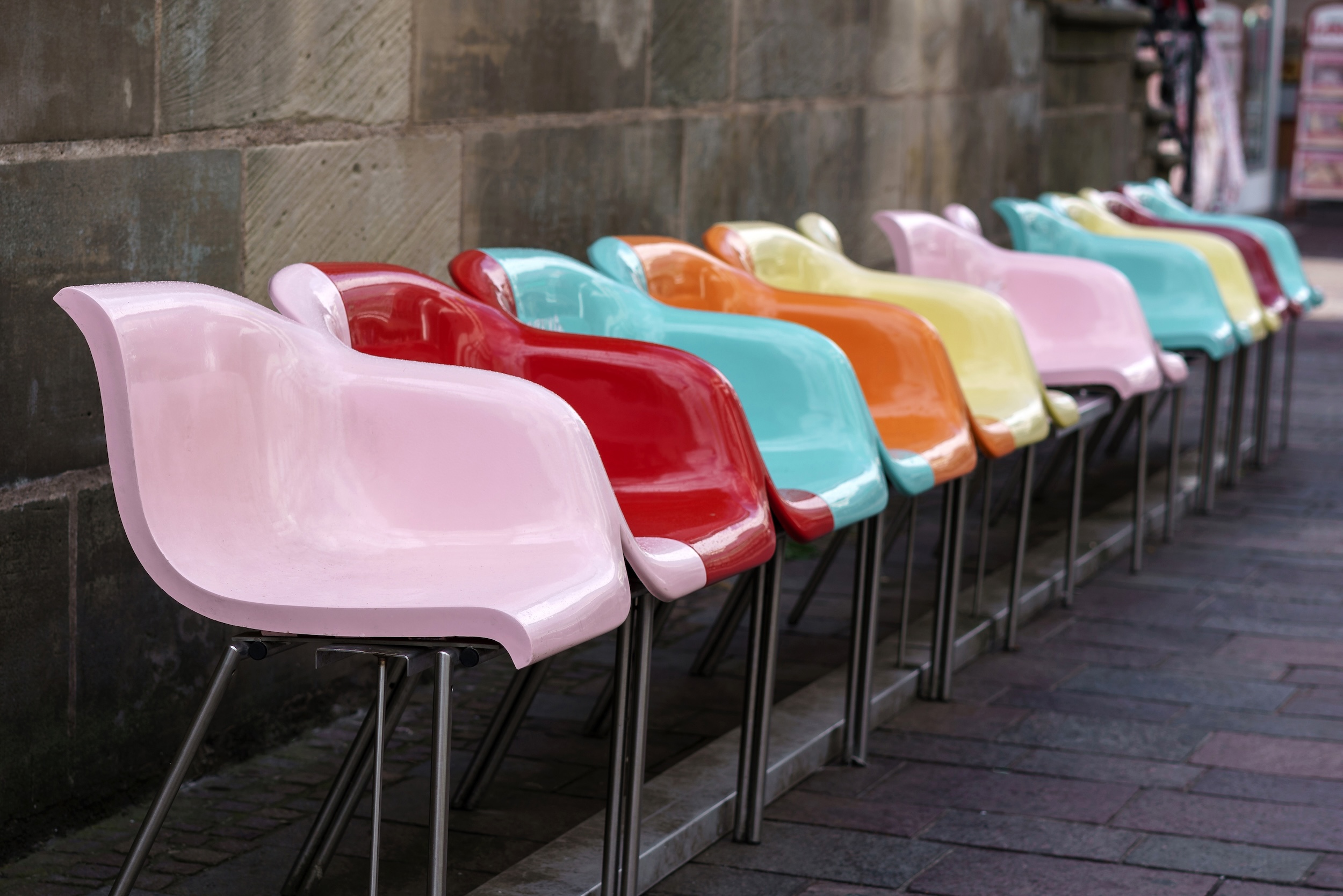 Multi-colored plastic seats in a row against a gray wall. Pedestrian area with empty colored seats.